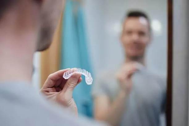 a man holding an Invisalign while looking at the mirror