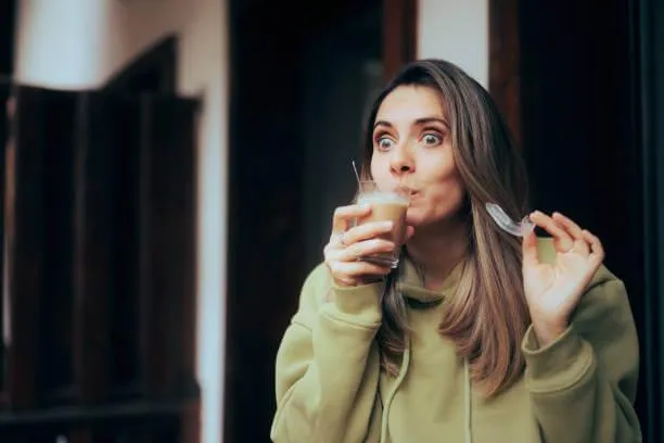a woman drinking coffee while holding her Invisalign