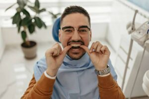 a man trying on his clear aligners while sitting on the dentist chair