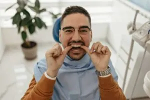 a man trying on his clear aligners while sitting on the dentist chair