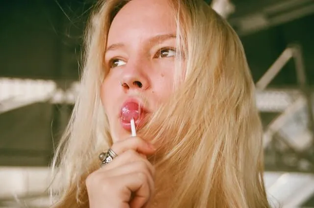 a woman with blonde hair sucking on a lollipop