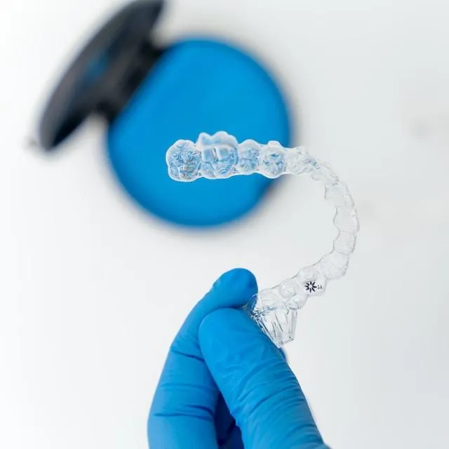 a hand in blue gloves holding an Invisalign