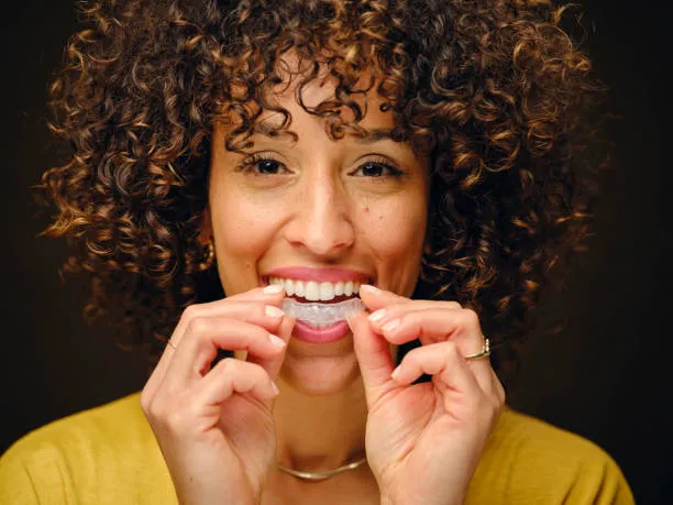 A happy young woman wearing a yellow top putting in her Invisalign