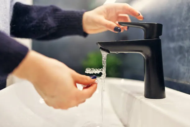 phot of a person's hands washing her Invisalign under running water