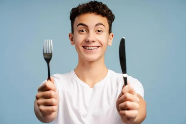 boy holding fork and knife looking at camera