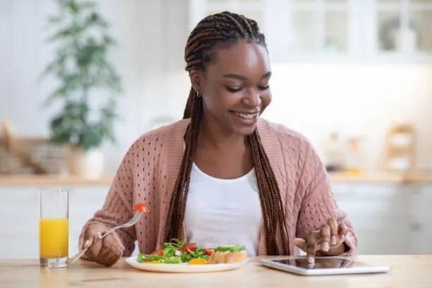 Woman Using Digital Tablet While Having Breakfast In Kitchen